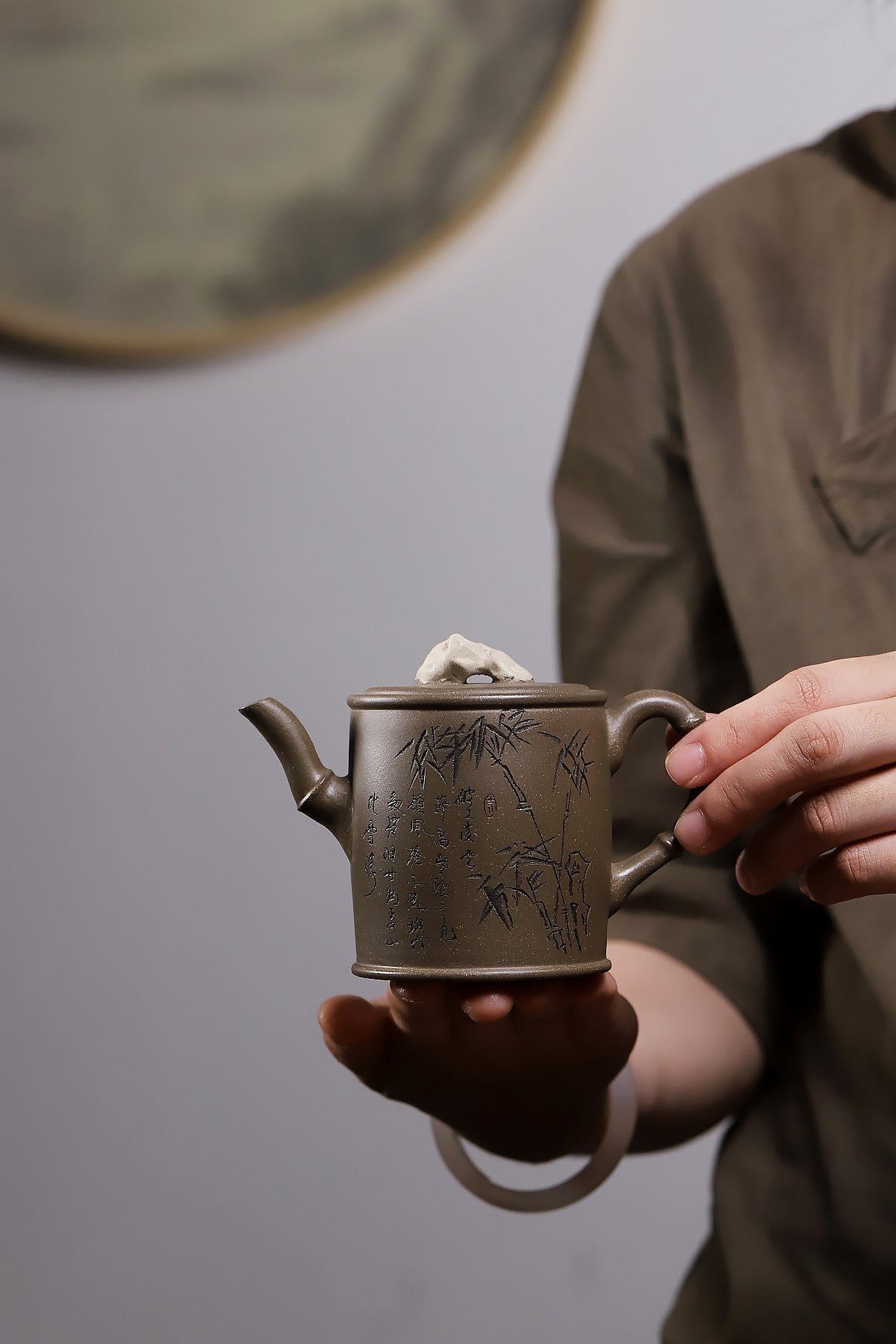 Grey-brown cylindrical teapot with bamboo decoration, held in two hands to show its size.