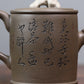 Grey-brown cylindrical teapot with bamboo decoration, close-up of calligraphy on the opposite side.