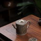 Grey-brown cylindrical teapot with bamboo decoration, viewed from above on a wooden table.