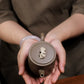 Grey-brown cylindrical teapot with bamboo decoration, overhead view while held in two hands.
