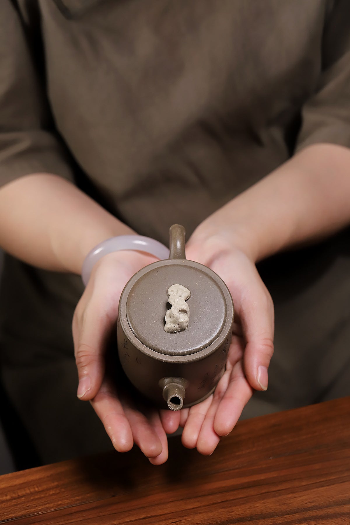 Grey-brown cylindrical teapot with bamboo decoration, overhead view while held in two hands.