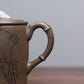 Grey-brown cylindrical teapot with bamboo decoration, bamboo-shaped loop handle close-up.