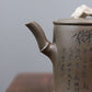 Grey-brown cylindrical teapot with bamboo decoration, bamboo-shaped spout close-up.