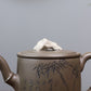 Grey-brown cylindrical teapot with bamboo decoration, close-up of the lid ornament and bamboo design.