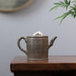 Grey-brown cylindrical teapot with bamboo decoration, opposite side showing calligraphy on a wooden table.