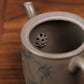 Grey-brown cylindrical teapot with bamboo decoration, interior close-up showing the perforated filter.