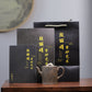Grey-brown cylindrical teapot with bamboo decoration, displayed in front of black packaging.