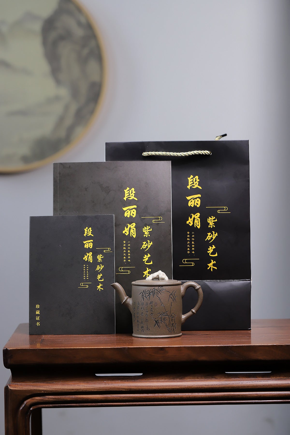Grey-brown cylindrical teapot with bamboo decoration, displayed in front of black packaging.