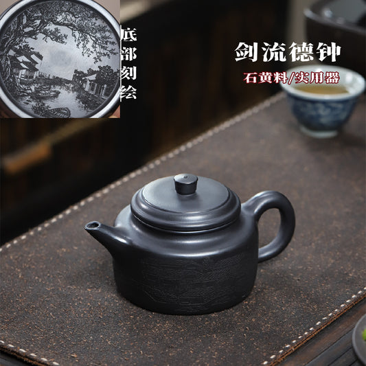 Black Dezhong teapot with engraved landscape, on a tea mat with Chinese text above.