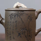Grey-brown cylindrical teapot with bamboo decoration, close-up of bamboo and Chinese characters on the body.