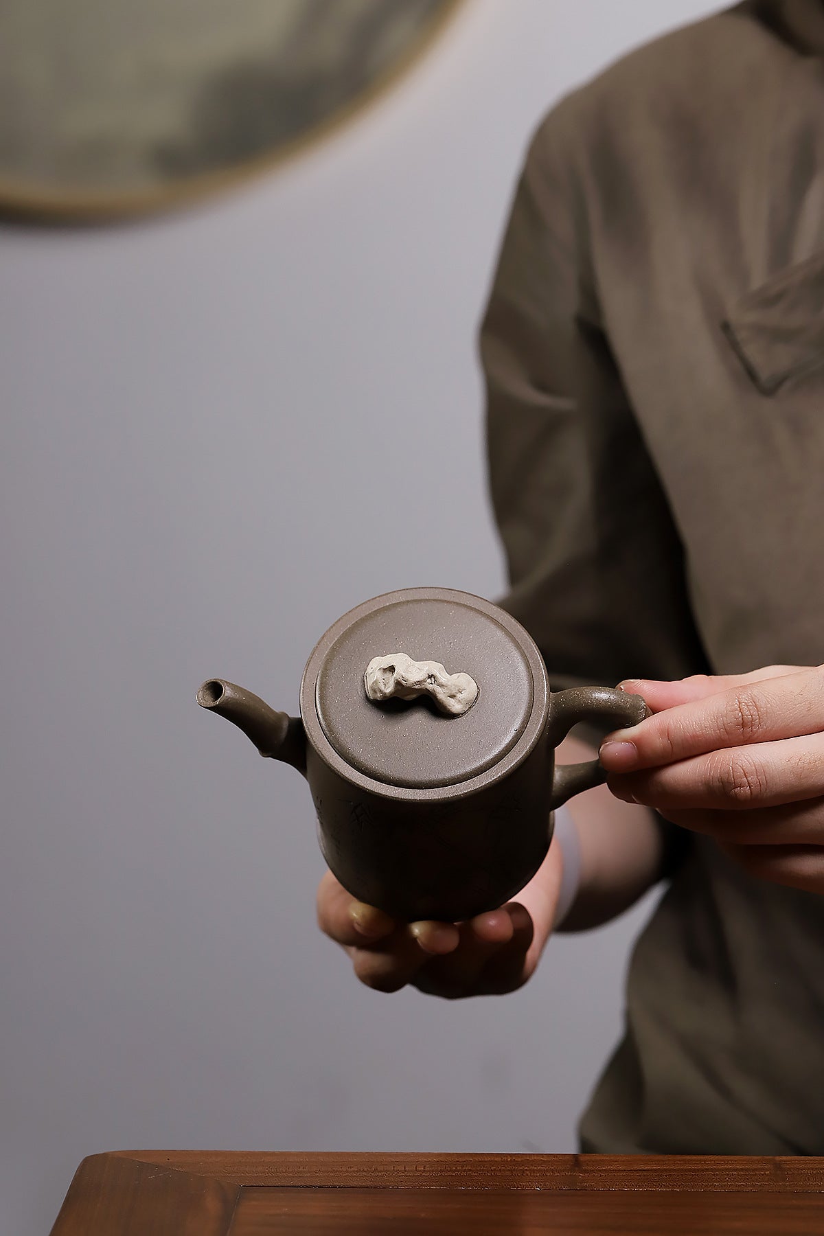 Grey-brown cylindrical teapot with bamboo decoration, top view while held in two hands.